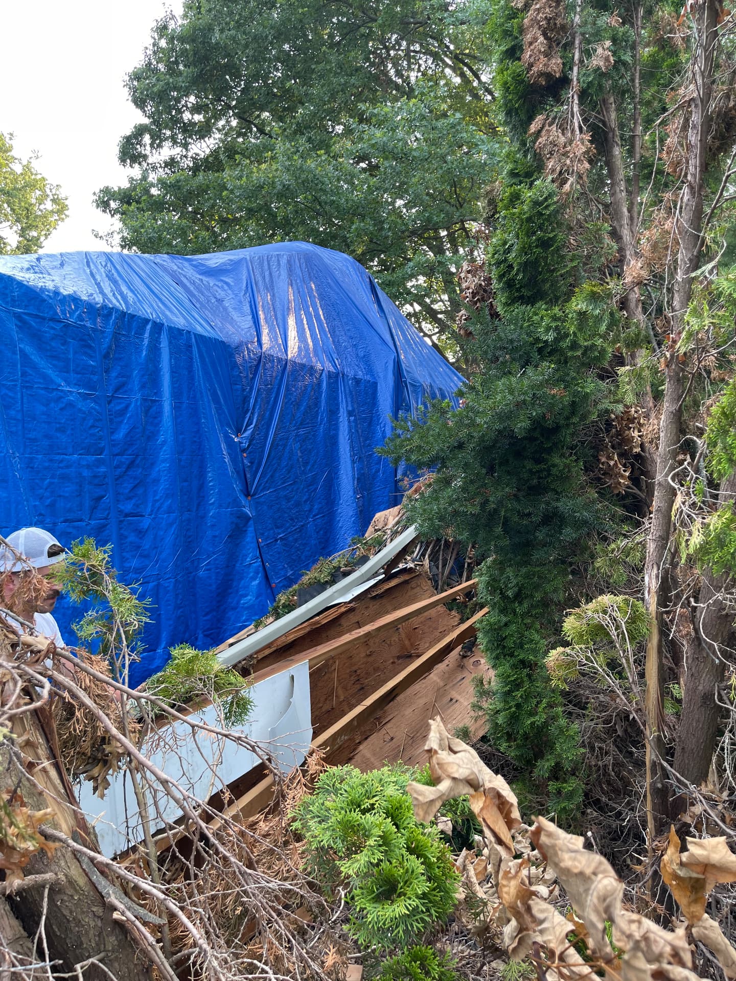 Tarped debris pile with fallen branches and broken lumber awaiting junk removal